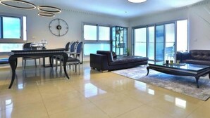 A spacious living room with a piano, a sofa, a coffee table, and a large window providing natural light. - Sea view family relax apartment (Netanya)