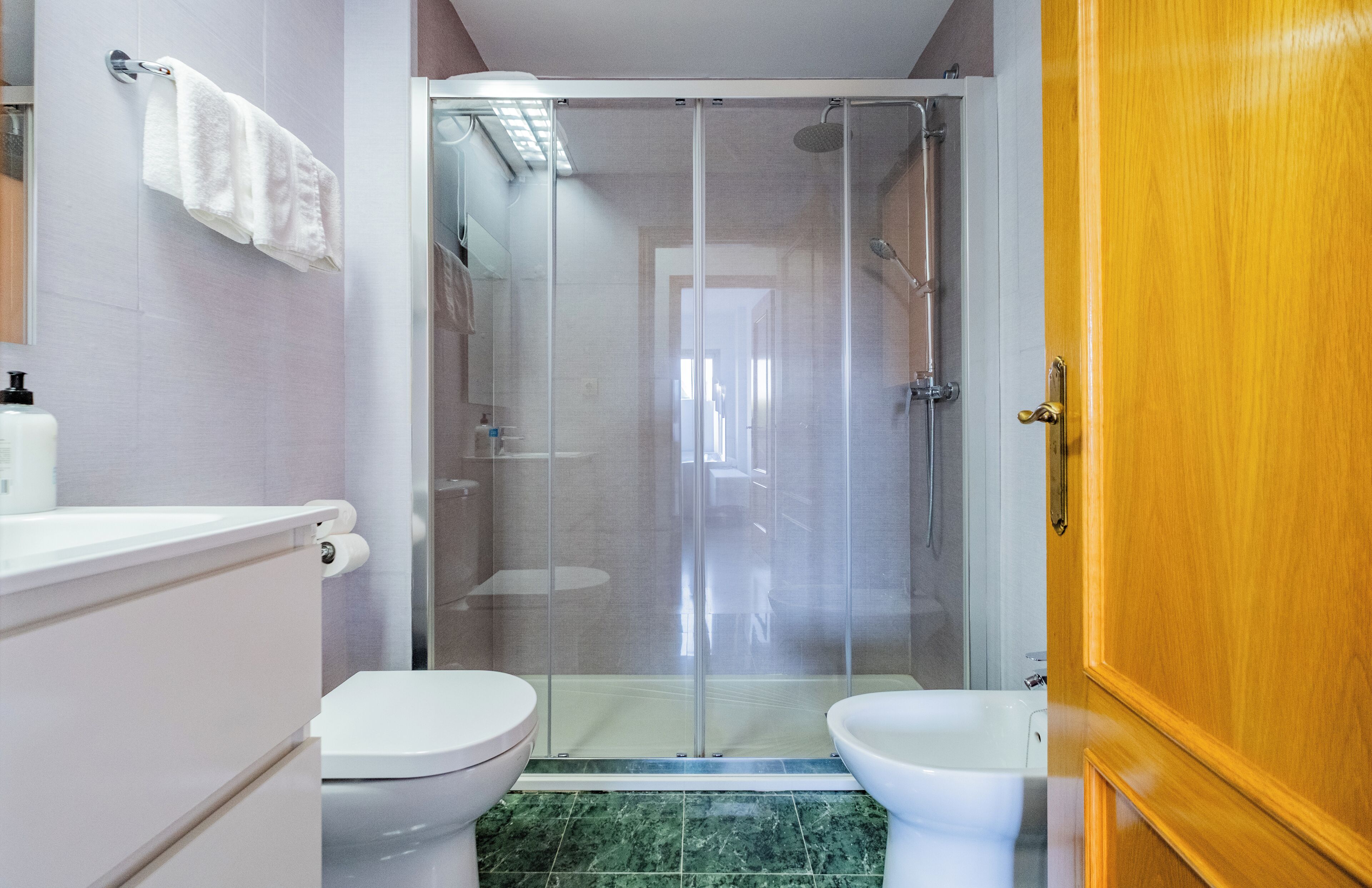 A bathroom with a glass-enclosed shower, two toilets, a sink, and a wooden door.