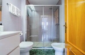 A bathroom with a glass-enclosed shower, two toilets, a sink, and a wooden door. - Apartamentos Proamar (Torre del Mar)