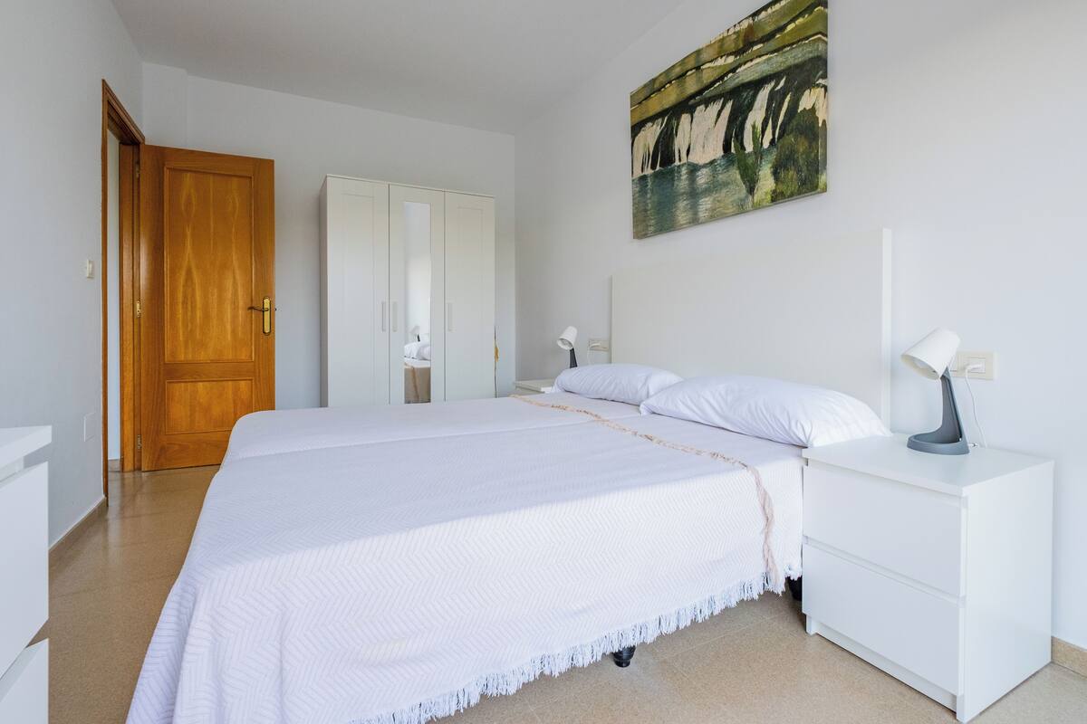A bedroom with a bed, nightstand, dresser, and a painting on the wall.