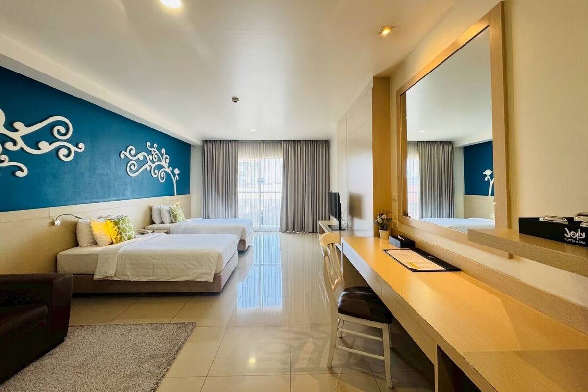 Une chambre d’hôtel avec deux lits, un bureau, une chaise, un grand miroir et un mur décoratif.