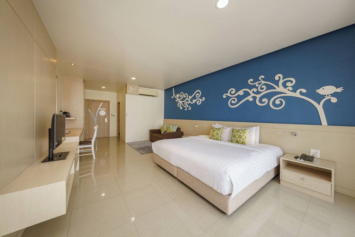 Une chambre d’hôtel moderne dotée d’un grand lit, d’une télévision, d’un bureau et d’un mur orné d’un motif décoratif représentant un arbre.