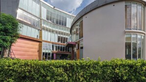A modern building with a curved glass facade, a flat roof, and a landscaped garden area. - Aspira Petchkasem (Krathum Baen)