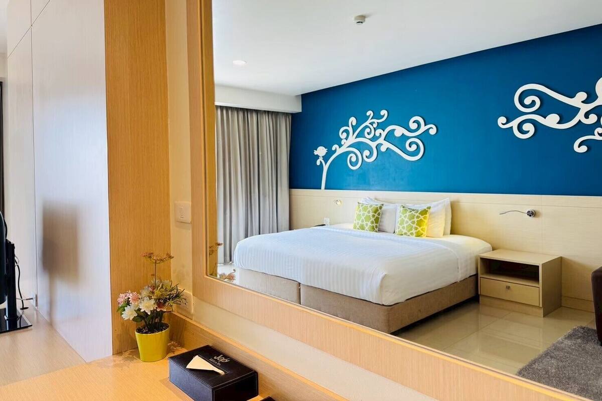 Une chambre d’hôtel moderne avec un grand miroir, un lit avec une literie blanche, un élément décoratif mural et une petite table de chevet.