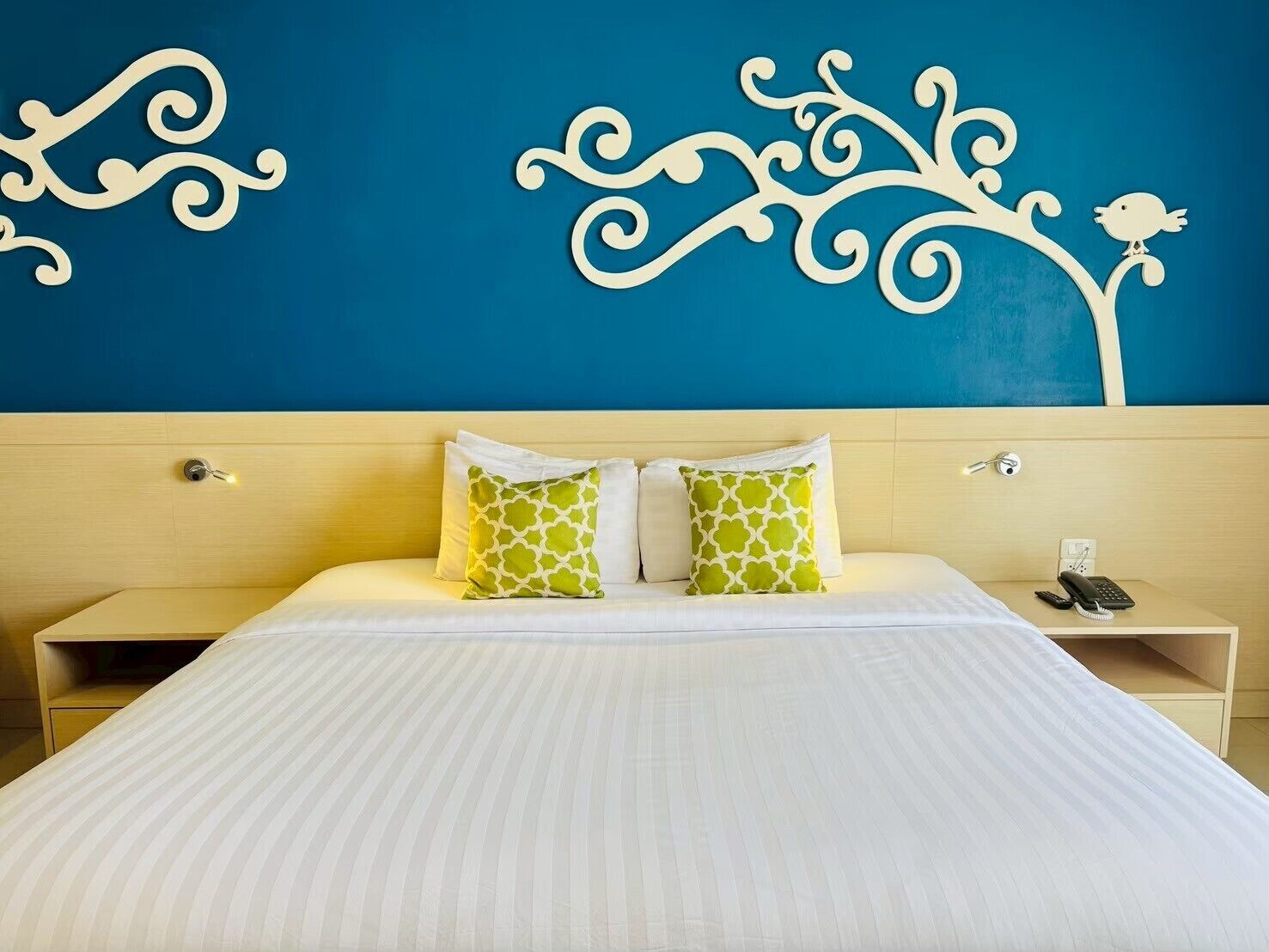 A hotel room with a bed, two pillows, a nightstand, a phone, and a wall decoration.
