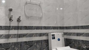 A bathroom with a toilet, a shower, and a towel rack. - Krishna Residency By Vrindavan Stays (Mathura)
