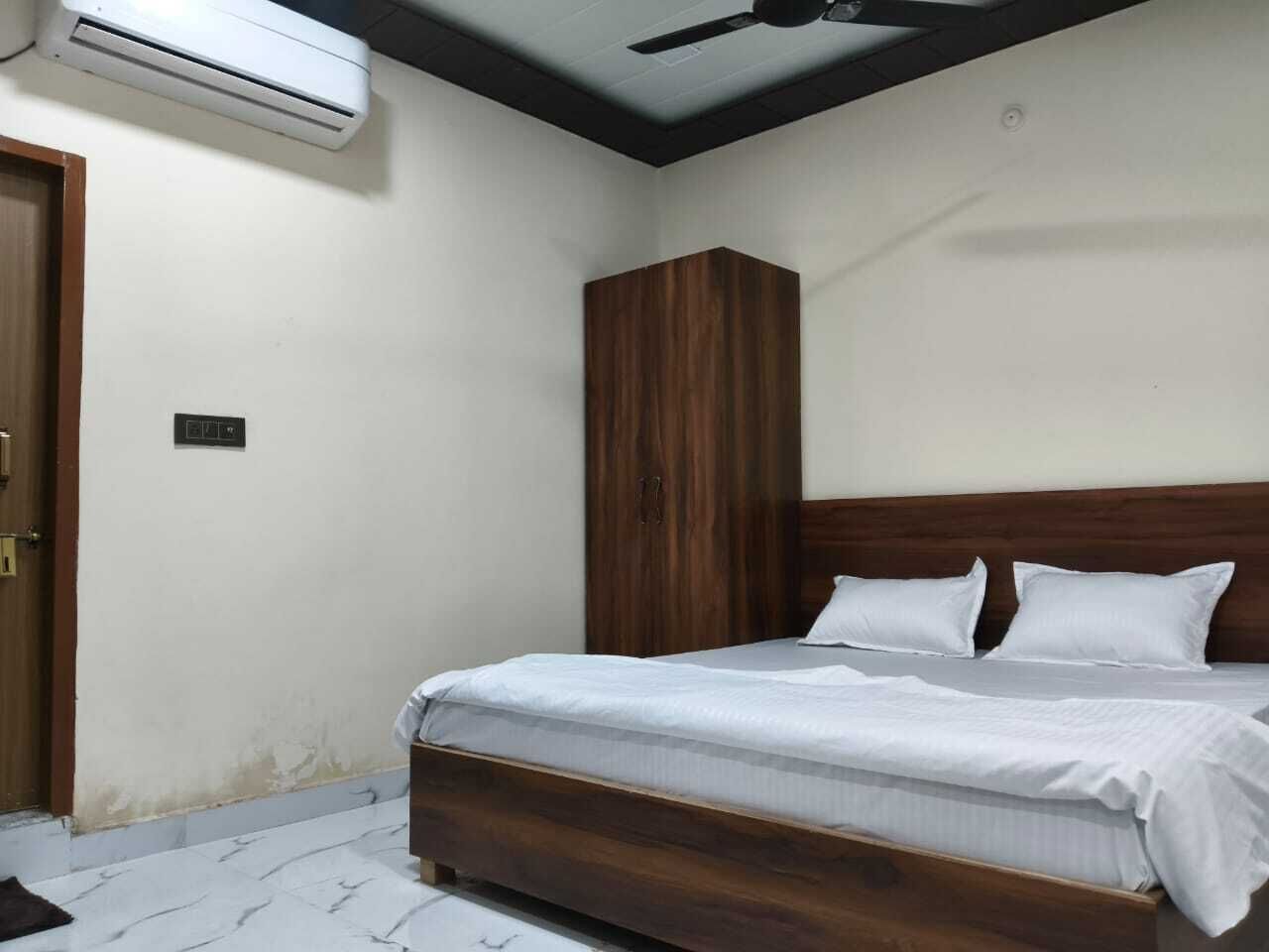 A bedroom with a wooden bed, white bedding, a wardrobe, and an air conditioning unit.