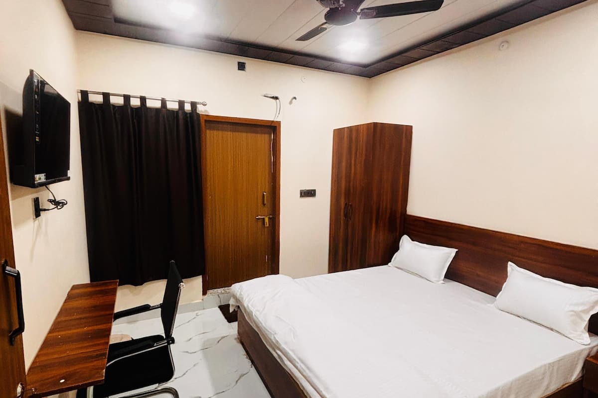 A bedroom with a bed, a desk, a chair, a television, and a ceiling fan.