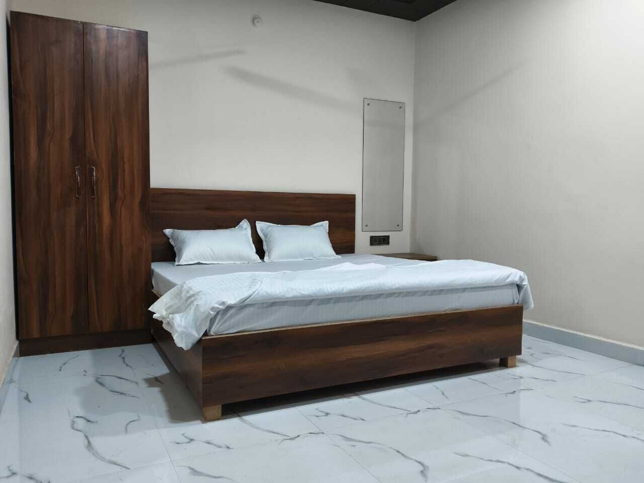 Un dormitorio con cama de madera, ropa de cama blanca, un armario y suelo de mármol.