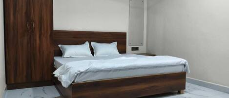 Un dormitorio con cama de madera, ropa de cama blanca, un armario y suelo de mármol.