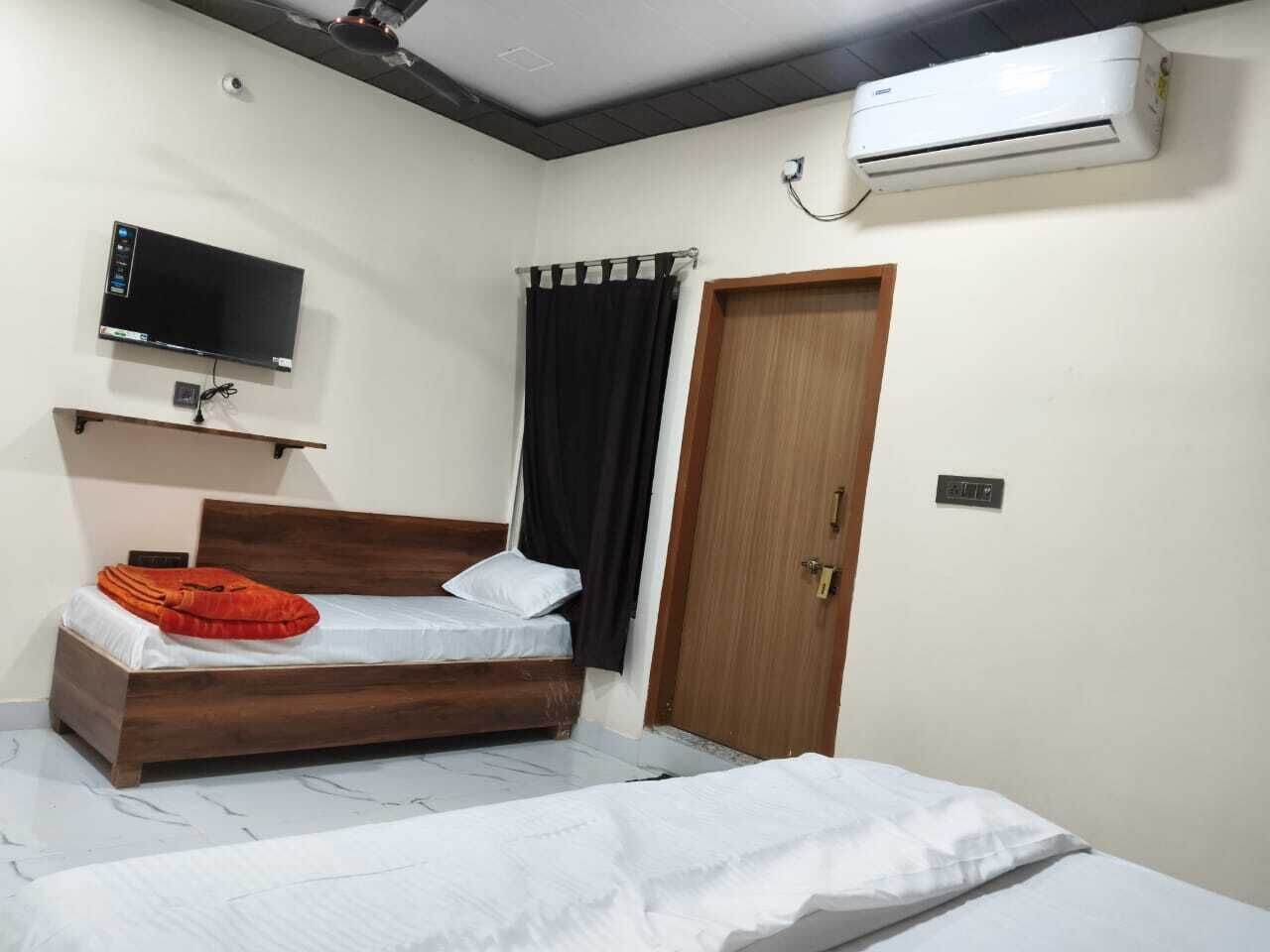 A bedroom with a bed, a TV mounted on the wall, an air conditioner, and a door.