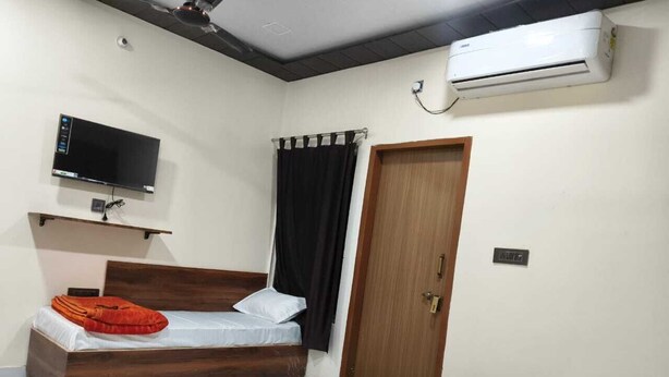 Un dormitorio con una cama, un televisor montado en la pared, aire acondicionado y una puerta.