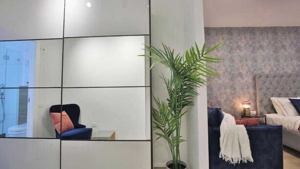 Un salon moderne avec un grand miroir, une plante en pot et un canapé doté d’une tête de lit capitonnée.