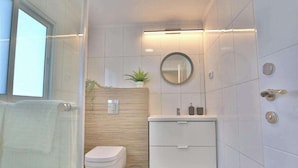 Une salle de bain moderne avec des toilettes, un lavabo et un miroir. Il y a une fenêtre sur la gauche et une plante accrochée au mur.