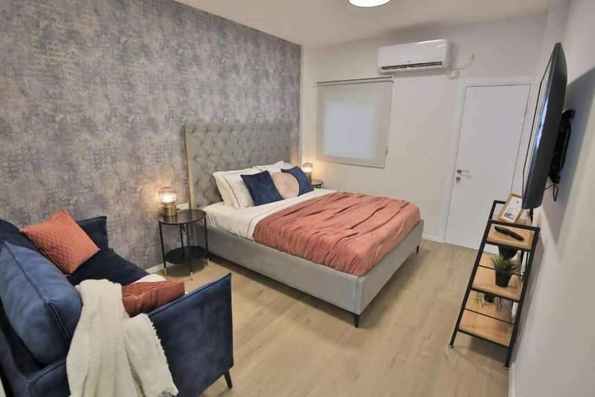 Un dormitorio moderno con cama, sofá, televisión y una mesita.