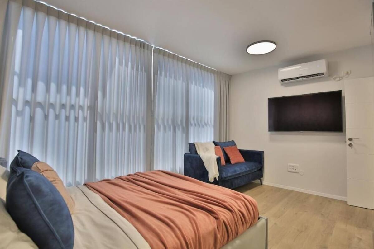Un dormitorio moderno con cama, sofá y televisor montado en la pared.