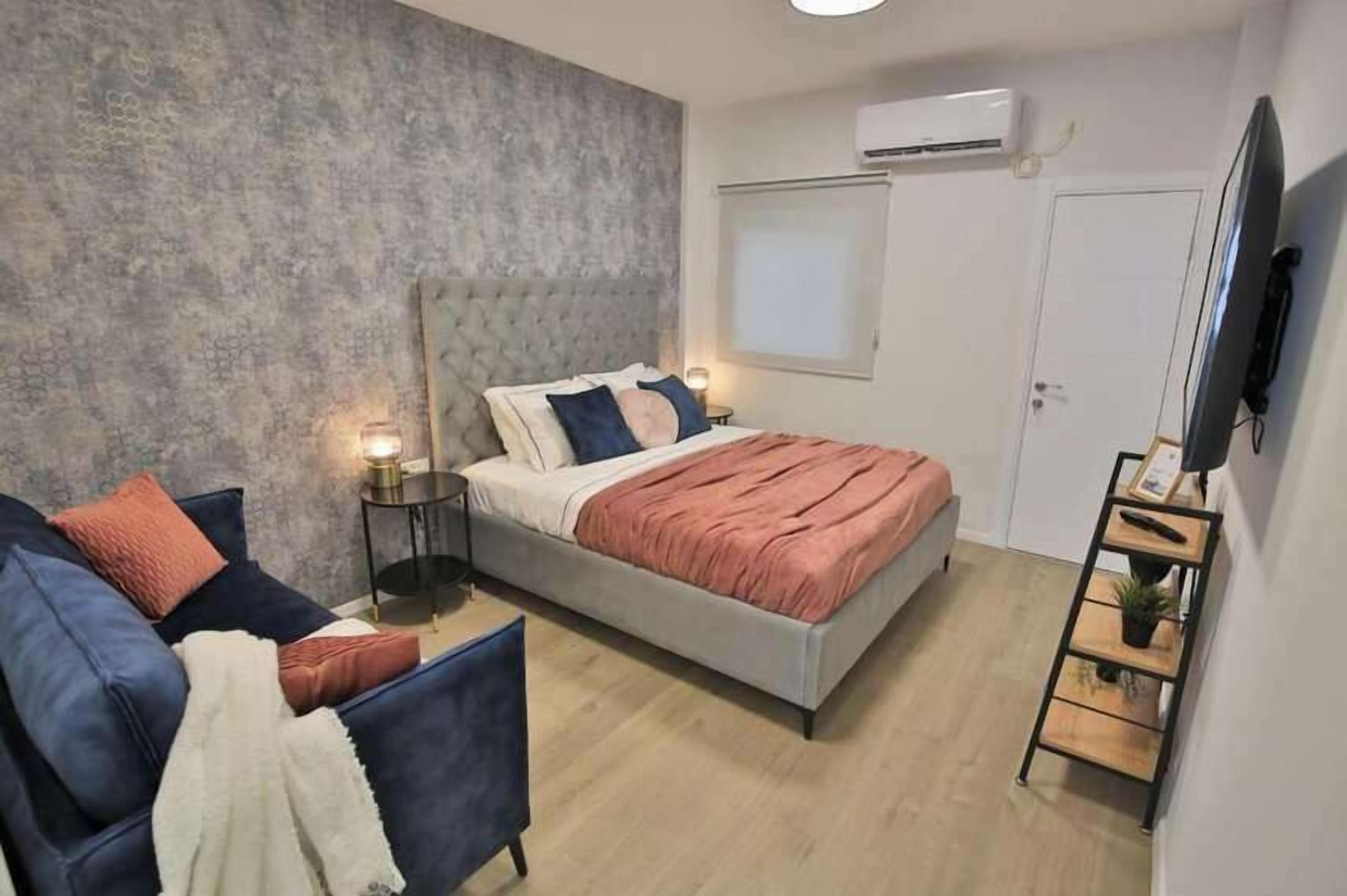 A modern bedroom with a bed, a sofa, a TV, and a small table.