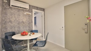 Une chambre moderne avec une table ronde, deux chaises, un saladier de fruits et un appareil de climatisation.