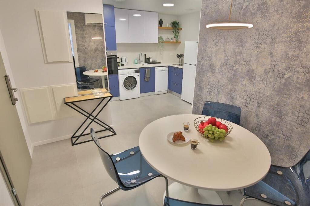 A compact kitchen with modern appliances, a dining area with a round table, and blue chairs.