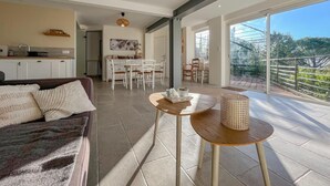 Un vaste espace de vie comprenant un canapé, une table à manger et des chaises, une cuisine à l’arrière-plan et une grande porte-fenêtre coulissante donnant sur un patio extérieur.