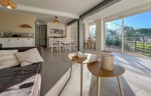 Ein geräumiger Wohnbereich mit einer Couch, einem Esstisch und Stühlen, einer Küche im Hintergrund und einer großen Schiebeglasdoor zum Außenbereich.