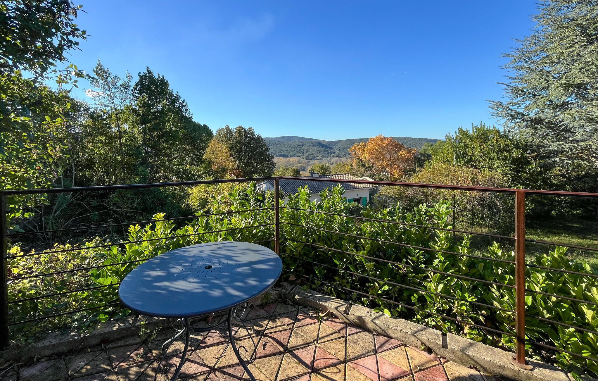 A patio with a round table and a view of a house and hills in the background.