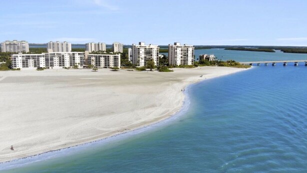 Un hotel frente al mar con varios edificios altos, una playa de arena y un puerto deportivo.