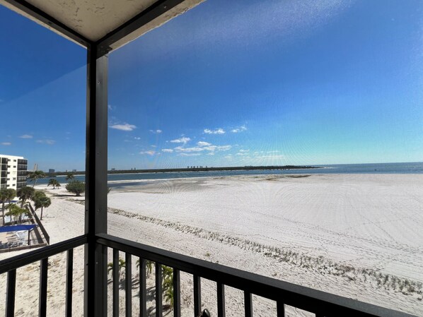 A beach view from a balcony with a railing, clear sky, and distant buildings. - Carlos Pointe 434 | 2BR/2BA, Renovated, Beachfront & pool (Fort Myers Beach)