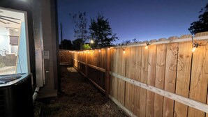 A wooden fence with string lights, a covered outdoor area, and a building entrance.