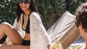 Una persona è sdraiata su una poltrona da spiaggia con bevande e snack accanto.