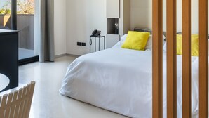 Una camera d'albergo moderna con un letto grande, una scrivania e una sedia. Si nota un telefono su un tavolino e una finestra con tende.