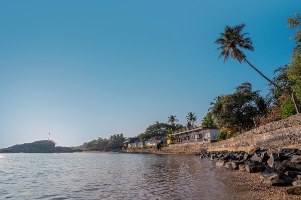 A coastal hotel with a rocky shoreline, palm trees, and a clear sky.
