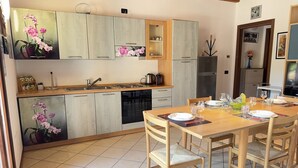 A modern kitchen with wooden cabinets, a dining table set for four, and a refrigerator. - Free Park and Swimming Pool, Centre of Peschiera (Peschiera del Garda)