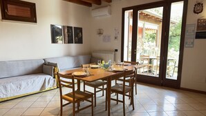 A dining area with a wooden table and chairs, a sofa, and a sliding glass door leading to an outdoor patio. - Free Park and Swimming Pool, Centre of Peschiera (Peschiera del Garda)