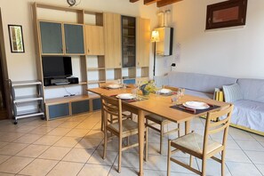 A dining area with a wooden table, chairs, and a TV. There are cabinets and shelves in the background. - Free Park and Swimming Pool, Centre of Peschiera (Peschiera del Garda)
