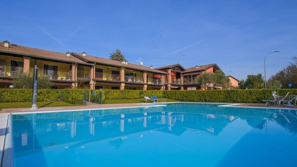 A swimming pool with lounge chairs, a building with balconies, and a clear blue sky. - Free Park and Swimming Pool, Centre of Peschiera (Peschiera del Garda)