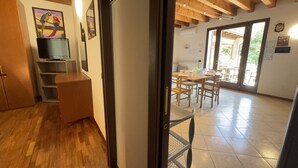 An interior with a wooden floor, a television on a stand, a dining area with chairs and a table, and a view through a door to an outdoor space. - Free Park and Swimming Pool, Centre of Peschiera (Peschiera del Garda)