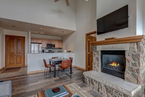 A spacious living area with a stone fireplace, a dining table with chairs, and a kitchen in the background. - Vail Valley Chapel Loft | Views & Walk to Gondola (Avon)