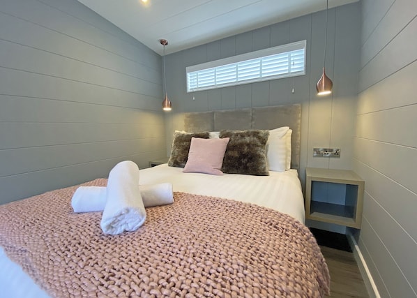 A modern bedroom with a large bed, a headboard, bedside tables, and a window with blinds.