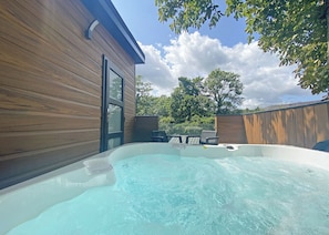 A hot tub in a backyard with a wooden house and a fenced area.