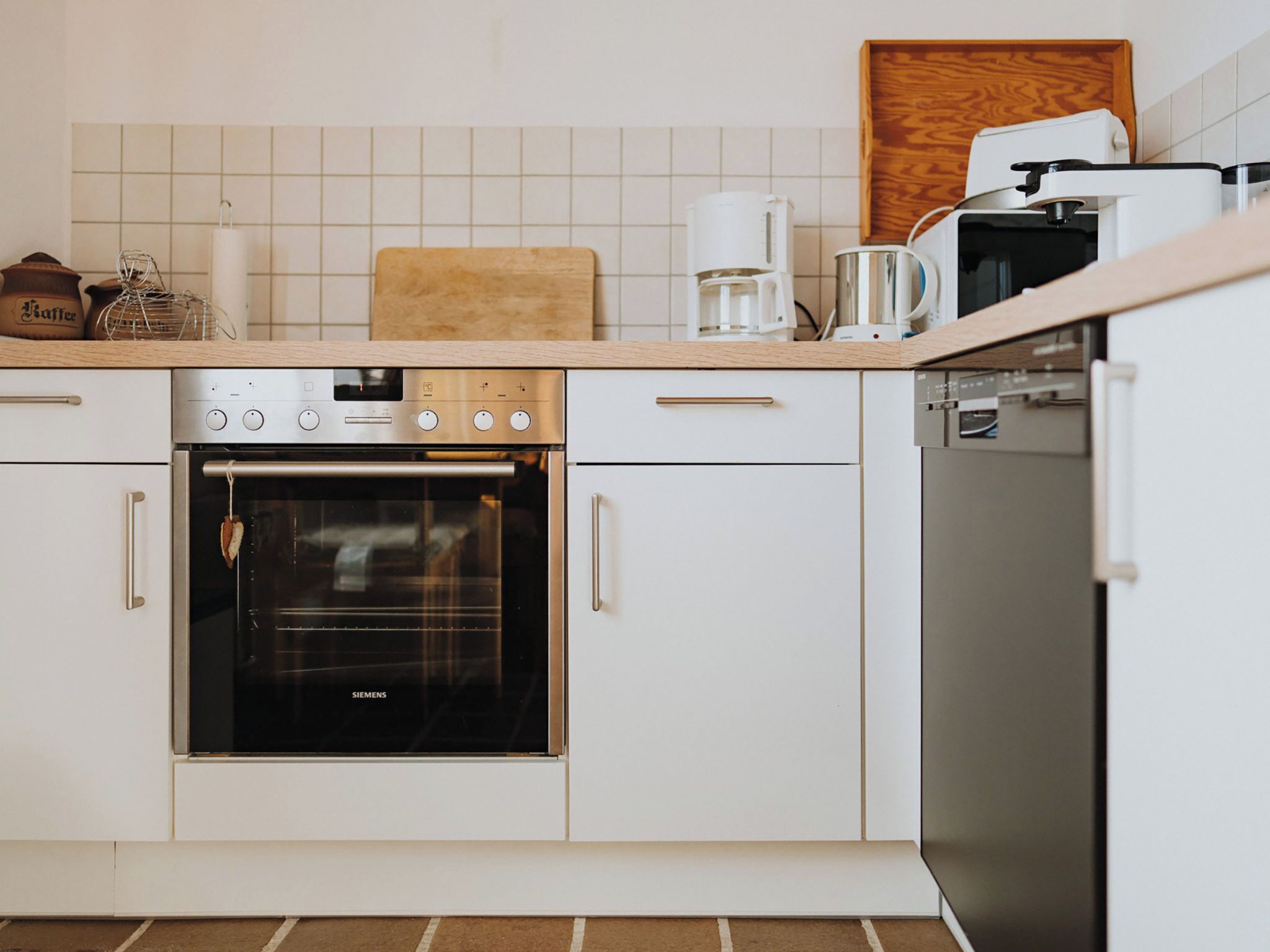 Une cuisine moderne avec des meubles blancs, un four Siemens, une machine à café et un lave-vaisselle.