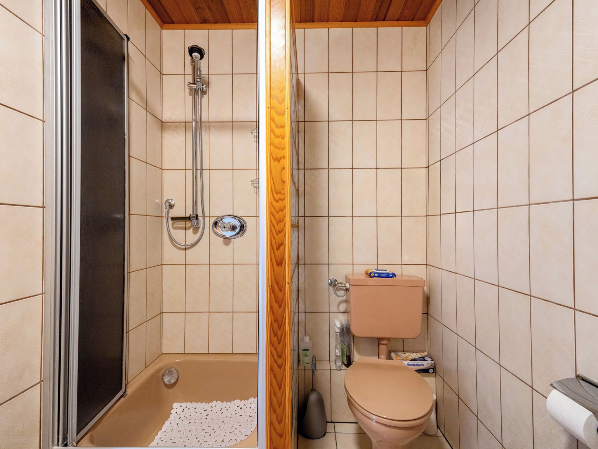 Un baño pequeño con ducha, inodoro y puerta de madera.