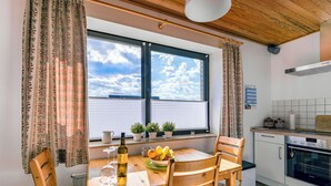 A dining area with a wooden table, chairs, a bottle of wine, and a bowl of fruit. There is a window with blinds and a view of the sky. - Teutoburger Wald 1 by Interhome (Schwalenberg)