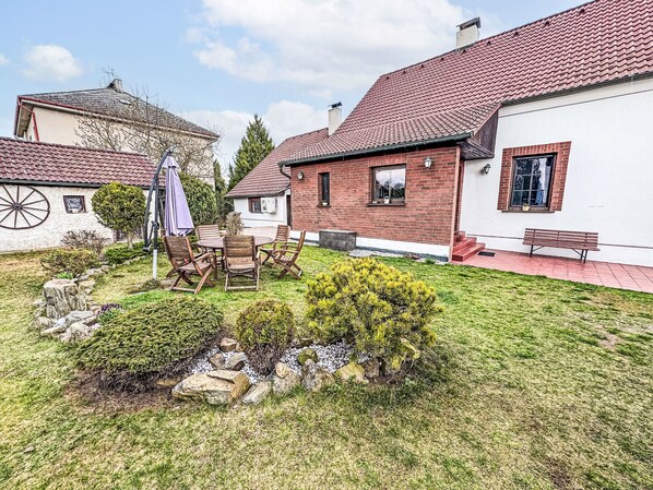 A courtyard with a round table and chairs, surrounded by a well-maintained lawn and a small garden area with rocks and shrubs.