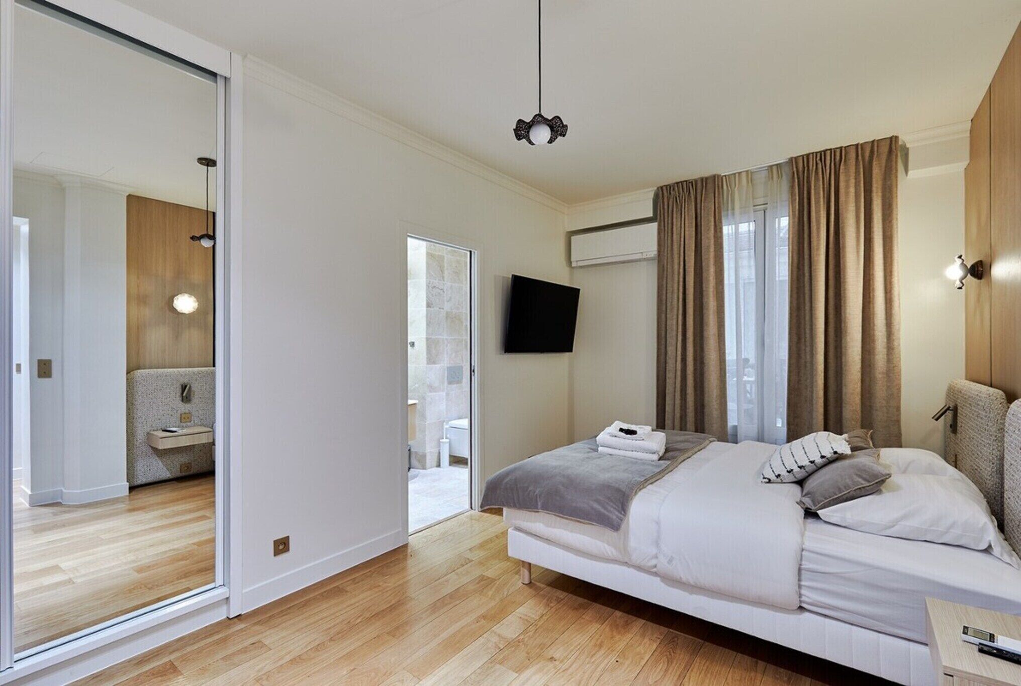 Un dormitorio moderno con una cama grande, un televisor de pantalla plana en la pared y una puerta corrediza de vidrio que da a un baño.