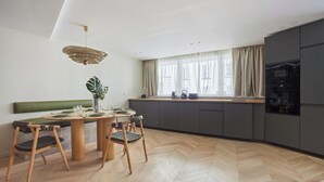 A modern kitchen with a dining area, featuring a herringbone wood floor, a green cushioned bench, a round wooden table, and a pendant light.