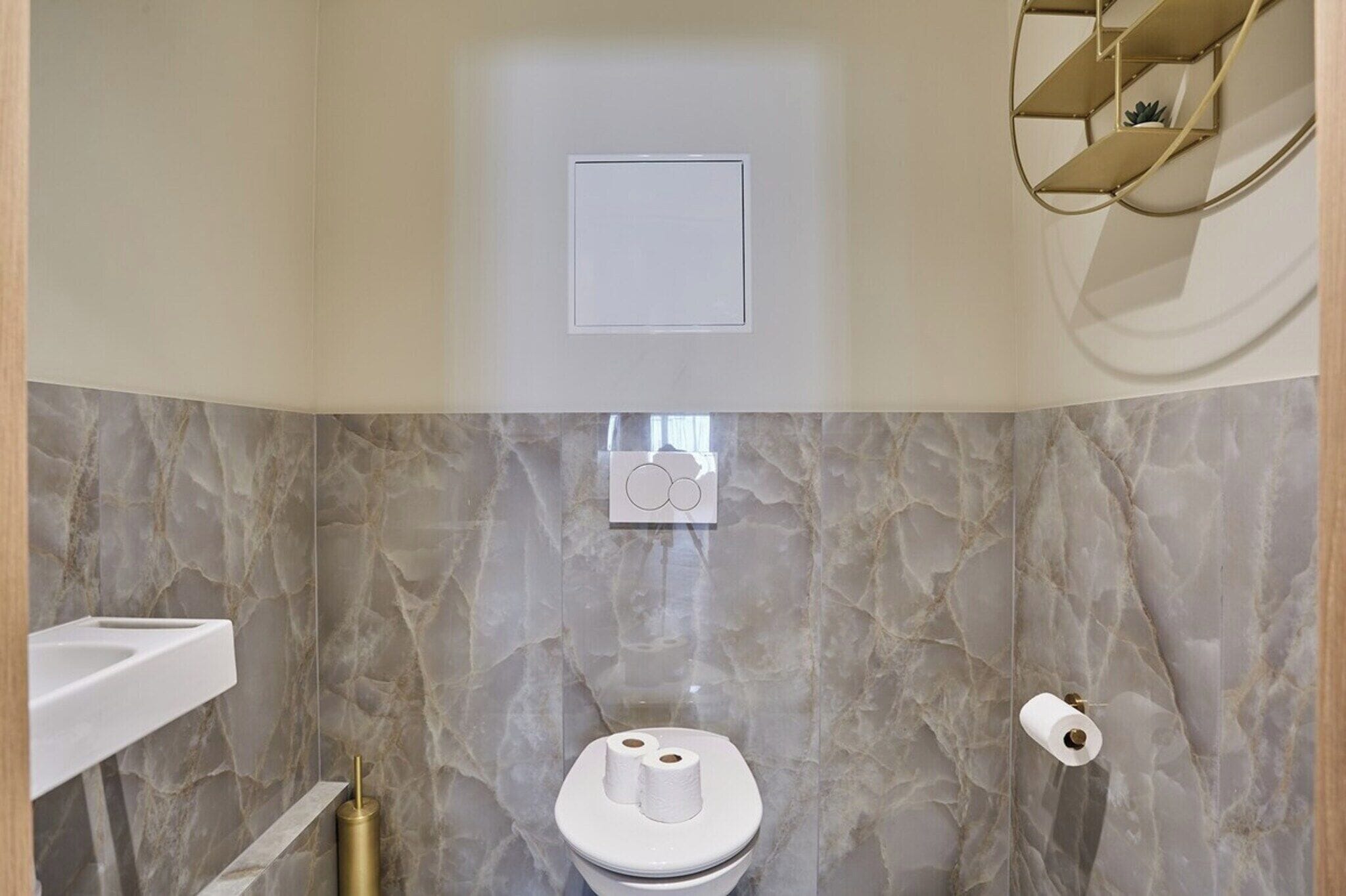 Une salle de bain avec un mur en marbre, des toilettes, un lavabo et un porte-rouleau de papier toilette.