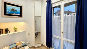 A room with a bed, a shelf with books and a plant, a framed picture, and a sliding glass door with curtains. - 3 bedroom awesome apartment in Peglio (Peglio)