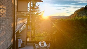 A balcony with a table and chairs, overlooking a forested landscape with a sunset. - 3 bedroom awesome apartment in Peglio (Peglio)