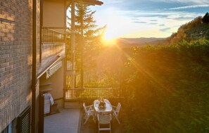 Ein Balkon mit Tisch und Stühlen, der einen Blick auf eine bewaldete Landschaft bei Sonnenuntergang bietet.